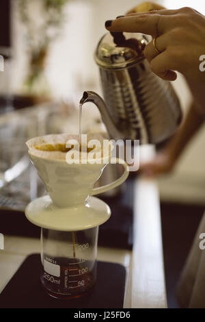 Femmina mani barista versando acqua calda attraverso imbuto in coffee shop Foto Stock