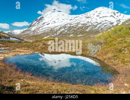 Alpine tarn, stagno riflette montagne dalle vette innevate sull'altro lato della parete di Troll, Norvegia Foto Stock