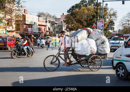 Locale indiana uomo pedalando un triciclo portando un grosso carico di sacchi in corrispondenza di un incrocio stradale in una strada trafficata nella Vecchia Delhi, Delhi, Punjab, India Foto Stock