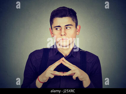 Subdolo furbizia offeso giovane uomo tramando qualcosa isolato sul muro grigio sfondo Foto Stock