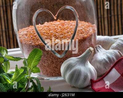 Cibo sano e jar con cuore motivi contenenti lenticchie rosse, un sano impulso commestibili legume, con garlics e rametto di menta open dalla finestra della cucina Foto Stock