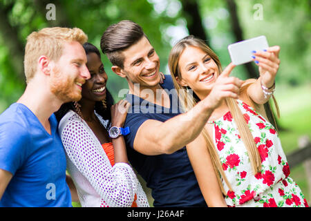 Un gruppo di giovani e coppie tenendo selfies nella natura e sorridente Foto Stock