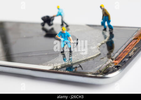 L'uomo in miniatura che fissa lo smartphone rotto, Close up shot Foto Stock