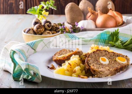 Foto orizzontale con la porzione del polpettone fatti in casa da carni suine e bovine carni macinate e riempita da uova di quaglia su piastra bianca con presa di patate. Altri Foto Stock