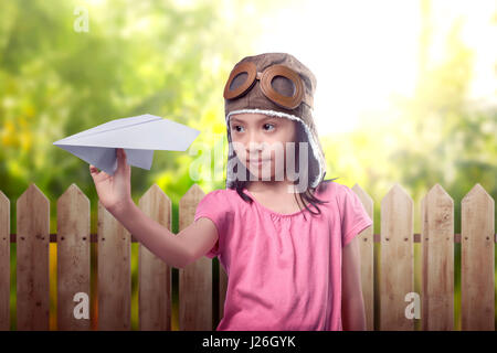 Funny asian bambina in aviatore casco giocando aeroplano giocattolo sul campo Foto Stock