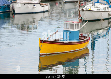 Un giallo barca scafo con una cabina blu sorge nelle calme acque del porto di Porthleven, Cornwall, Regno Unito Foto Stock