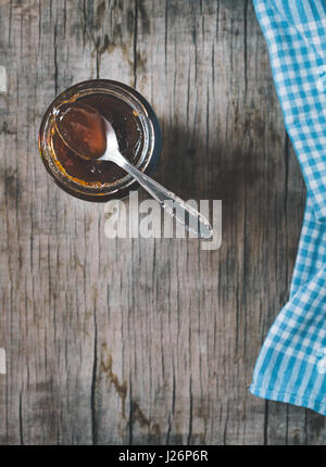 Cucchiaio e il vasetto di vetro di marmellata sul vecchio tavolo in legno. Tonica foto. Foto Stock