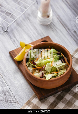 Fresca insalata mista servita in un piatto di argilla su un tavolo di legno. Foto Stock