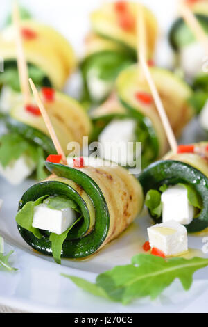 Deliziosi involtini di zucchine fritte e le fette di formaggio feta con rucola, servita con olio di oliva e pezzi di peperoni Foto Stock