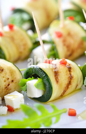 Deliziosi involtini di zucchine fritte e le fette di formaggio feta con rucola, servita con olio di oliva e pezzi di peperoni Foto Stock