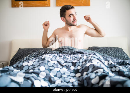 Un giovane uomo di svegliarsi nel letto e stirando le braccia Foto Stock