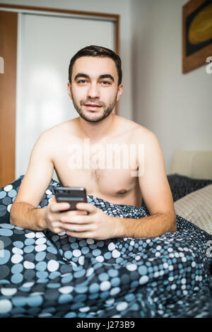 Uomo disteso nel letto di mattina con il telefono cellulare utilizzando l'app o la lettura di notizie Foto Stock