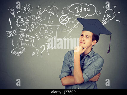 Giovane uomo bello con graduazione hat cerca fino a pensare l' istruzione ha molte idee sulla vita futura isolato sul muro grigio sfondo Foto Stock