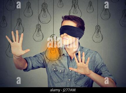 Gli occhi bendati giovane uomo a piedi attraverso le lampadine alla ricerca per la brillante idea Foto Stock