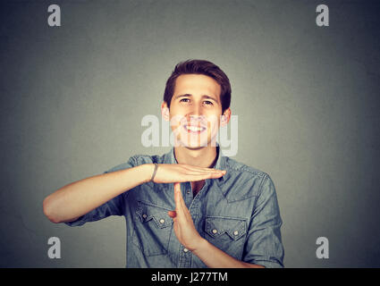 Uomo felice dando tempo fuori mano gesto isolato sul muro grigio sfondo Foto Stock