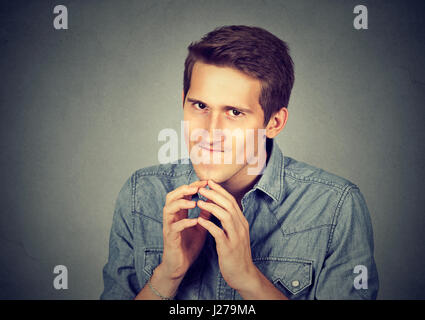 Subdolo intrigante giovane uomo tramando qualcosa isolato sul muro grigio Sfondo. Negativo emozione umana espressione facciale sensazione atteggiamento Foto Stock