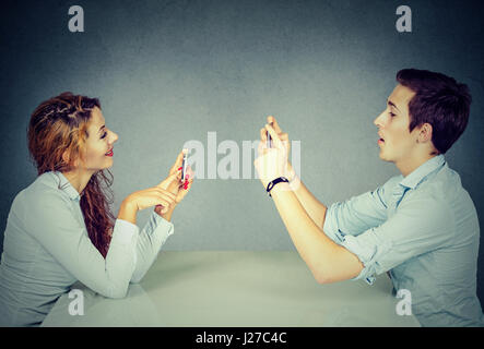 Giovane uomo e donna seduta al tavolo utilizzando i telefoni cellulari, i messaggi di testo tramite reti sociali con ossessionato espressione o scattare foto di ogni altro Foto Stock