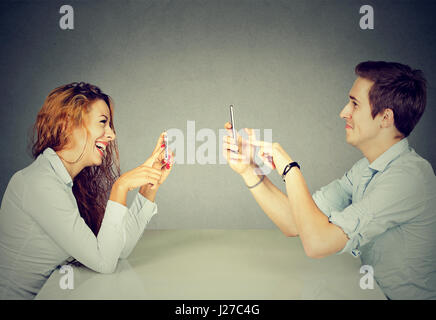 Giovane uomo e donna seduta al tavolo utilizzando i telefoni cellulari, i messaggi di testo tramite reti sociali con ossessionato espressione o scattare foto di ogni altro Foto Stock