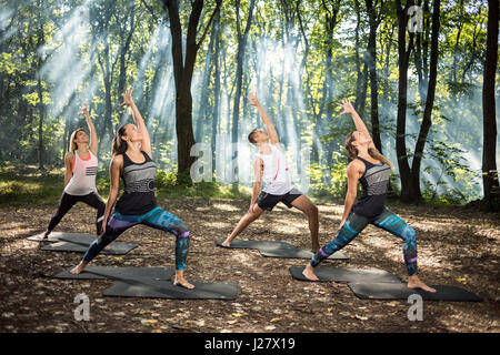 Un gruppo di donne di eseguire semplici esercizi di stretching in sun foresta illuminata Foto Stock