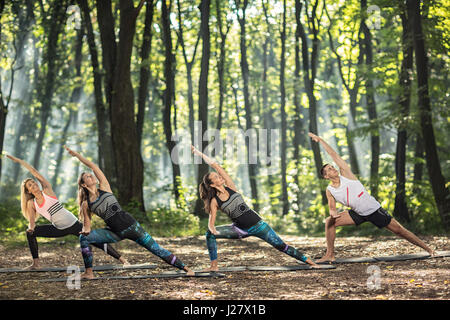 Un gruppo di giovani eseguita Facile esercizi fisici guardando il cielo attraverso le corone di alberi in foresta Foto Stock