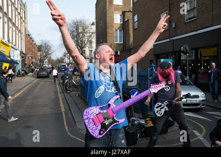 Due uomini in Portobello Road eseguire le loro prestazioni musicista di strada a heavy rock musica mentre finge di giocare giocattolo di plastica chitarre in London, England, Regno Unito. Uno ha un Guitar Hero uno, mentre gli altri una rosa di Hannah Montana di chitarra. Foto Stock