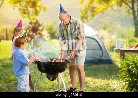 I bambini e il nonno avente un barbecue sul campeggio Foto Stock