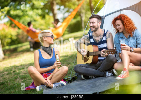 Tatuaggio giovane ragazzo suonare la chitarra mentre le ragazze gode in Musica e birra fredda al Summer Camp Foto Stock