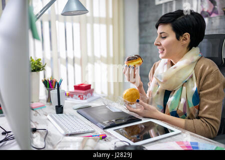 Designer soddisfatti mangiando ciambelle in office Foto Stock