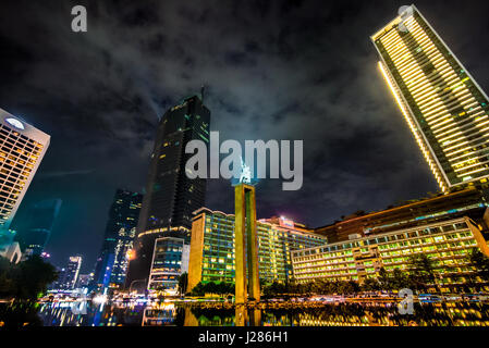 Monumento di Benvenuto nel cuore di Jakarta di notte circondato da edifici alti nella zona conosciuta come Bundaran HI. Foto Stock