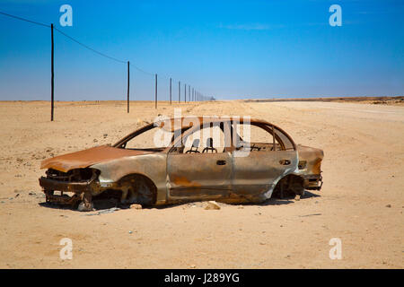 Infinite strada di ghiaia il C35 e devastata auto Namibia regione desertica Foto Stock
