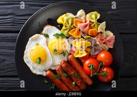 Uova fritte, salsicce, farfalle di pasta e pomodoro close-up su una piastra. Vista orizzontale dal di sopra Foto Stock