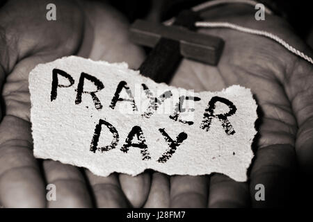 Primo piano delle mani di un giovane uomo caucasico con un crocifisso in legno e un pezzo di carta con il testo di preghiera nel giorno di loro Foto Stock