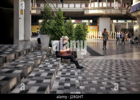 Donna di prendere una pausa dal lavoro e sat leggendo il giornale al di fuori sulla strada. Bangkok, Thailandia, Foto Stock