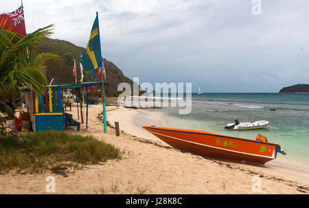 Capanna sulla spiaggia e bandiere internazionali con un taxi d'acqua, spiaggia e vista dei Caraibi: Salt Whistle Bay, Mayreau, Saint Vincent e Grenadine. Foto Stock