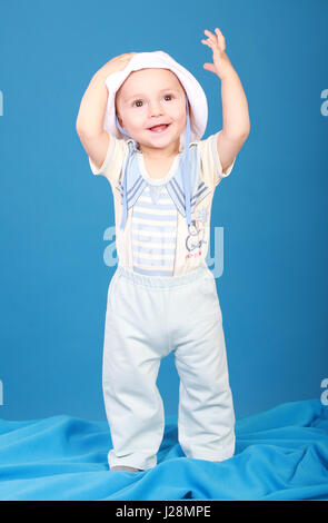 Il capretto nel sailor suit lì in piedi sorridente, alzando la mano verso l'alto. Sfondo blu Foto Stock