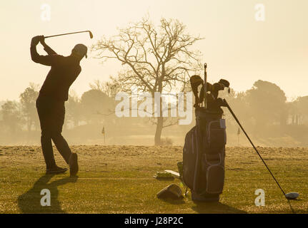 Gli amanti del golf swinging golf club in inizio di mattina di sole su una pratica gamma di guida all'alba. Foto Stock