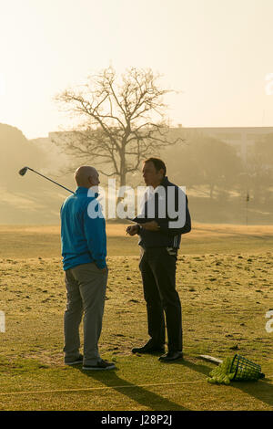 Gli amanti del golf swinging golf club in inizio di mattina di sole su una pratica gamma di guida all'alba. Foto Stock