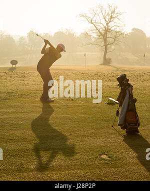 Golf club oscillante al sole di prima mattina sul campo pratica all'alba - ombra lunga. Foto Stock
