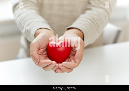Ravvicinata di un uomo anziano con cuore rosso in mani Foto Stock