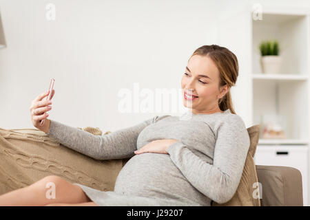 Donna incinta prendendo selfie smartphone a casa Foto Stock