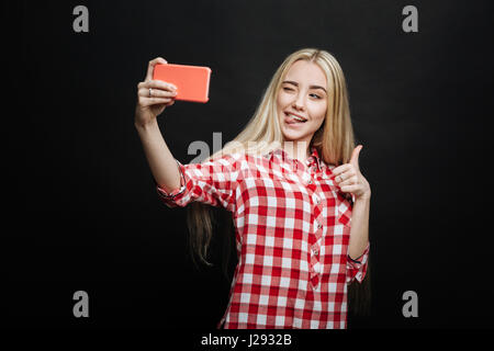 Vivace adolescente tenendo selfie su sfondo nero Foto Stock