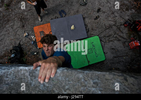 Un scalatore di pietra lo tenta di appendere la sommità di un masso a Fontainebleau, Francia, dopo saltando da mantiene al di sotto di Foto Stock