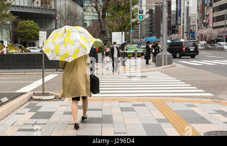 Tokyo, Giappone - 8 aprile 2017: Donna che cammina in tokio indossa trench coat, borsa nera e ombrello con motivo floreale. Foto Stock