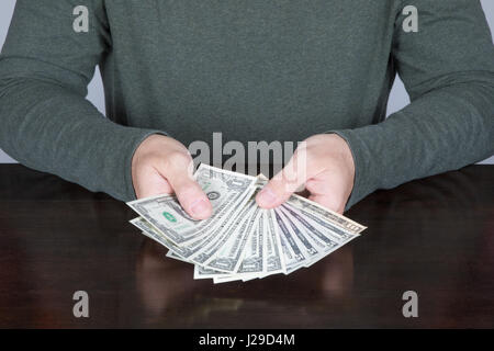 Le mani di uomo con camicia verde che mostra o la valuta di conteggio denaro in contanti, una di cinque e dieci dollari di banconote nel corso di legno marrone scuro e tabella Foto Stock
