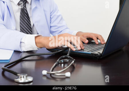 Lo stetoscopio è sdraiato sul tavolo vicino medico maschio digitando su computer notebook - assistenza medica e sanitaria concetto Foto Stock