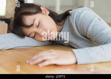 Stanco studente asiatica ragazza dorme sul tavolo. studiare, educazione, sessione di esami e il concetto di scuola. Foto Stock