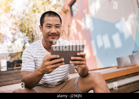Sorridente uomo asiatico seduto sulle scale al di fuori di un tablet Foto Stock