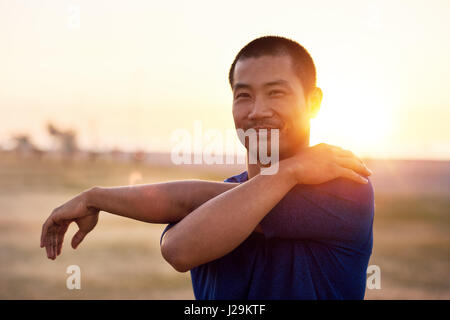 Montare il giovane uomo asiatico stretching braccia prima di una corsa Foto Stock