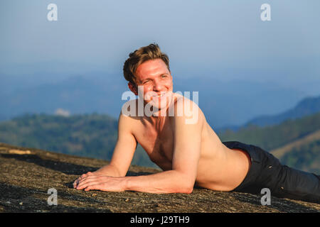 Athletic uomo sorridente si trova sulla cima di una montagna. Il turista riposa dopo la scalata. Foto Stock