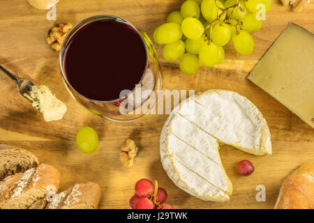 Un overhead foto di un bicchiere di vino rosso con una selezione di formaggi, pane e uva Foto Stock